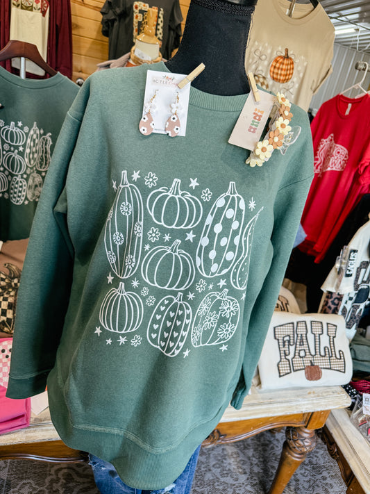 Sage green LAT drop hem crewneck sweatshirt featuring white whimsical pumpkin illustrations with floral, heart, and polka dot patterns, styled as a trendy fall boutique outfit.