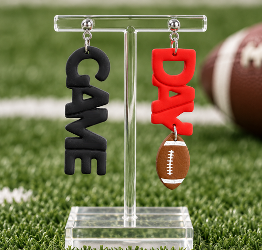 Game Day football statement earrings featuring black GAME lettering, red DAY lettering, and a dangling brown football charm with silver-tone ball studs, perfect for football season and tailgating.