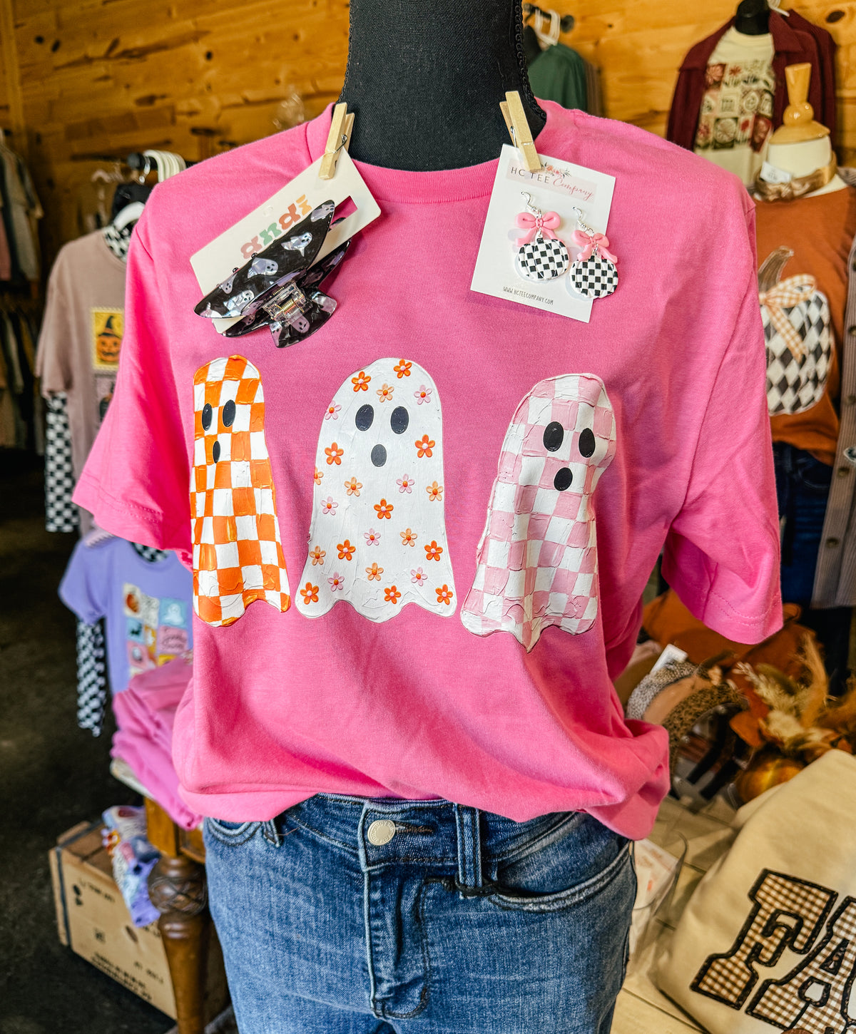 Pink Bella Canvas Halloween graphic t-shirt featuring three retro ghosts with orange checkerboard, floral, and pink checkerboard patterns. Cute spooky season boutique tee.