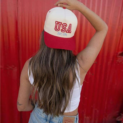Woman wearing a red and white embroidered USA trucker hat with patriotic stars design and “Est. 1776” detail against a red background. Perfect patriotic baseball cap for Fourth of July, Memorial Day, and summer Americana style.